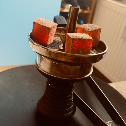 A cozy setup featuring a sleek hookah surrounded by vibrant flavor jars and glowing coals on a wooden table.