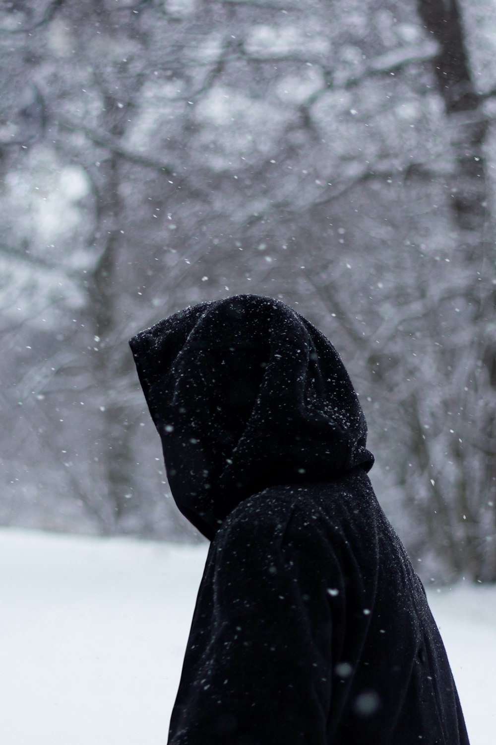 pessoa em capuz preto em pé no chão coberto de neve durante o dia