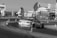 A sports car is drifting around a track surrounded by traffic cones. The background features a building with signs and banners, indicating an event or roadshow. The scene appears to be at an organized racing or motorsport event.