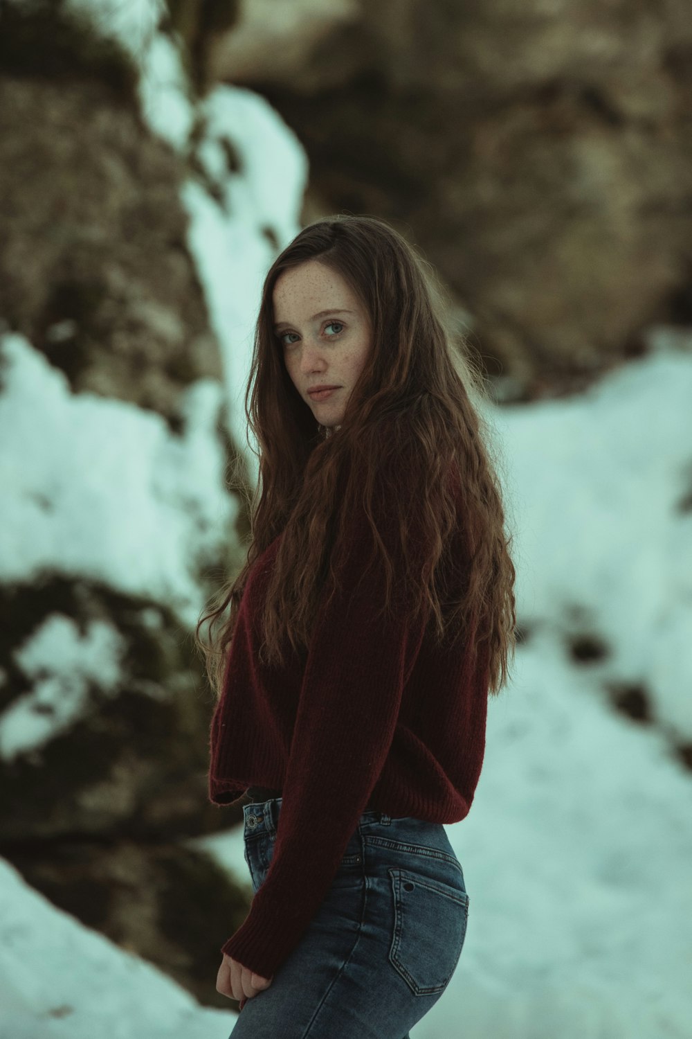 mulher na camisa vermelha de manga comprida e jeans jeans azuis em pé no chão coberto de neve durante