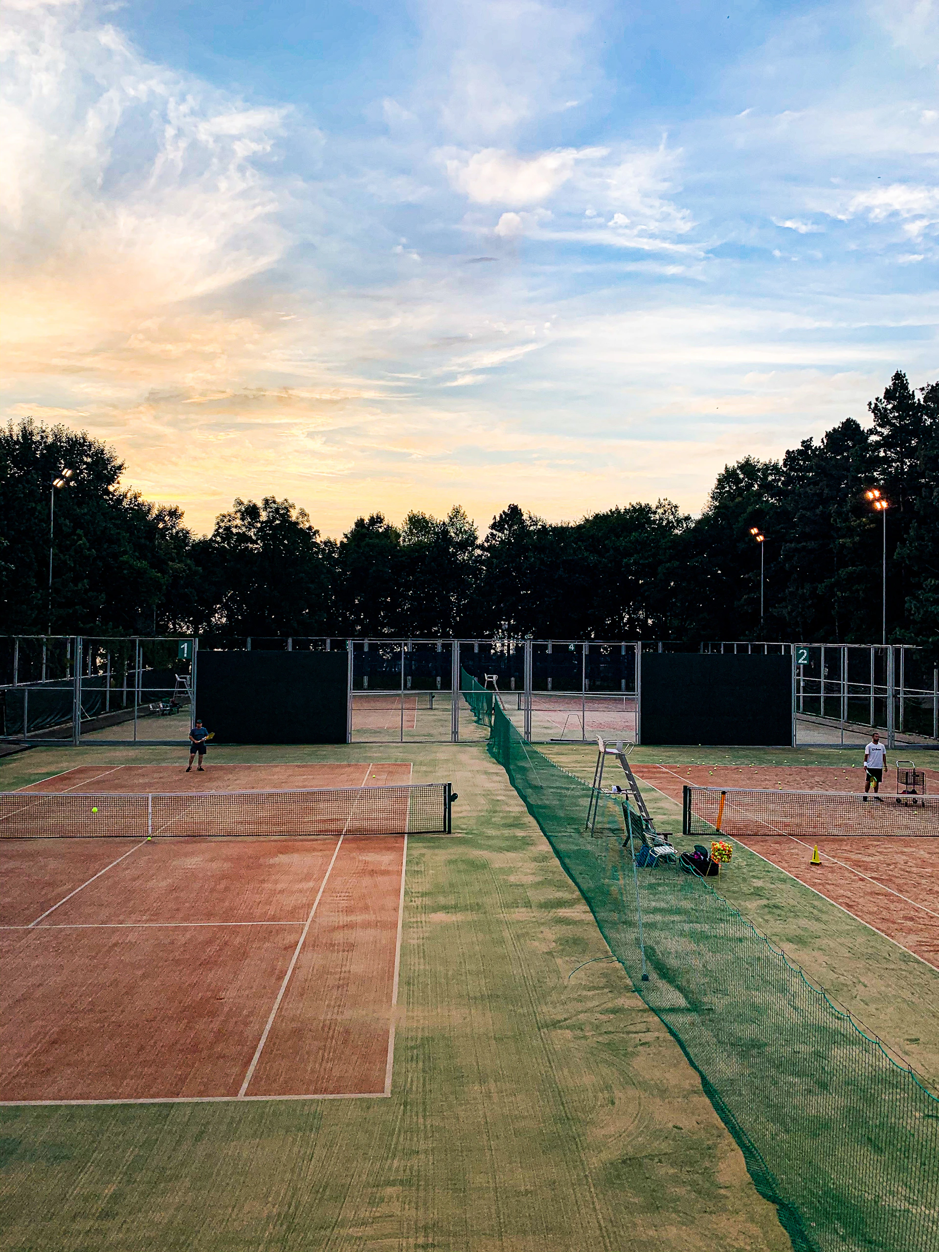 Photo of a lively tennis match underway on one of raquetaviva's clay courts at sunset, with players focused and the net glowing under warm light.