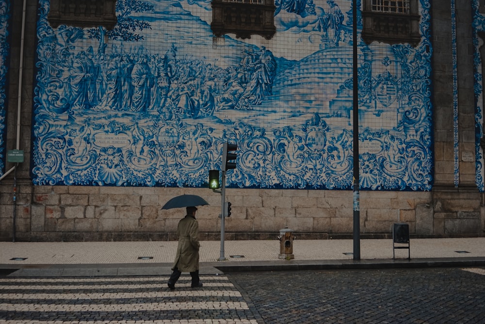 person in gray coat holding umbrella walking on sidewalk during daytime