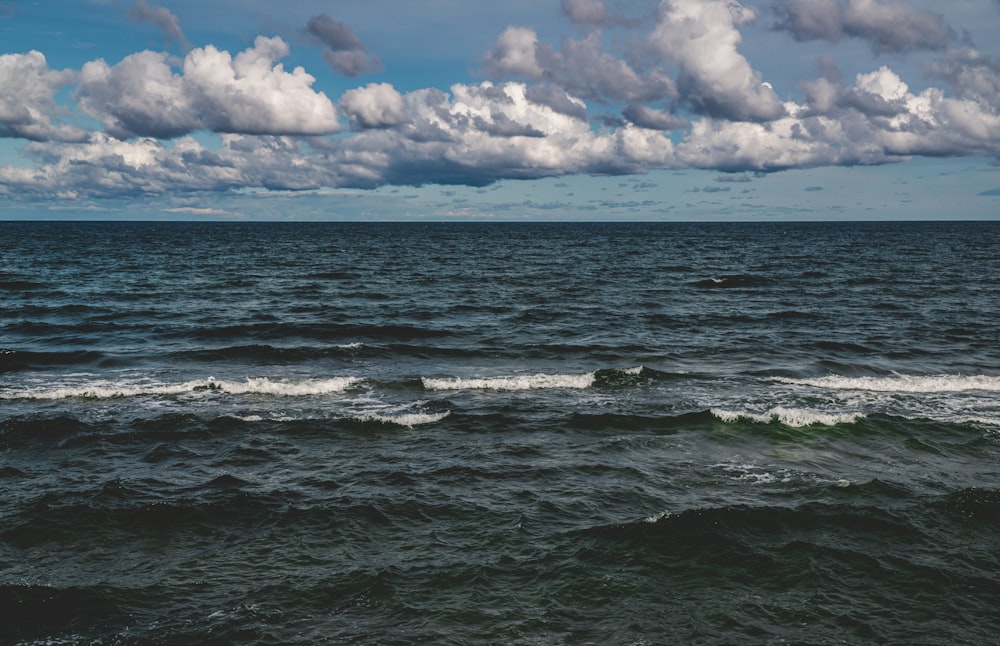 ocean waves under white clouds and blue sky during daytime