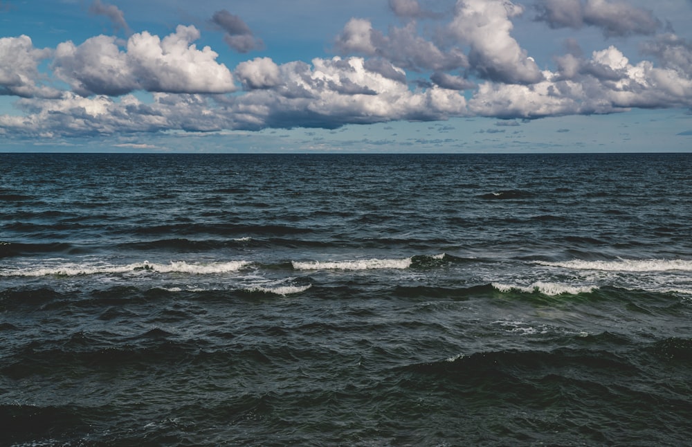 olas del océano bajo nubes blancas y cielo azul durante el día