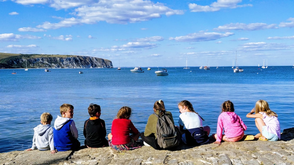 group of people sitting on rock formation near body of water during daytime