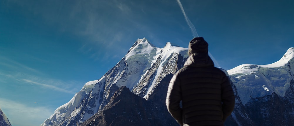 Hombre con sudadera con capucha a rayas negras y grises de pie cerca de la montaña cubierta de nieve durante el día