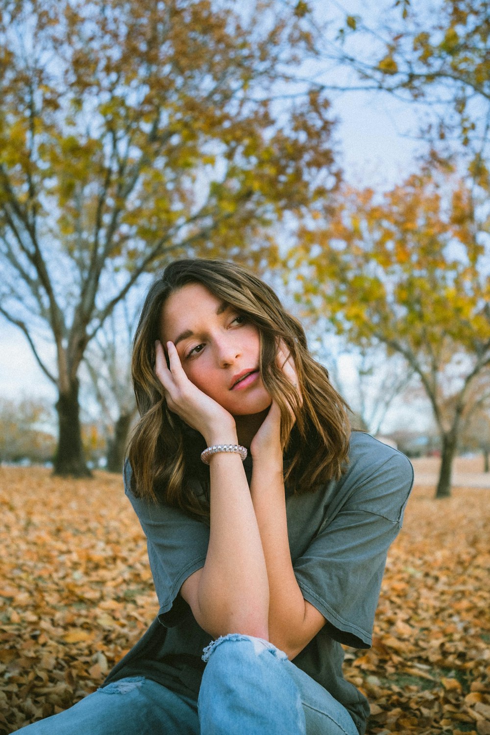 woman in gray shirt sitting on brown dried leaves during daytime