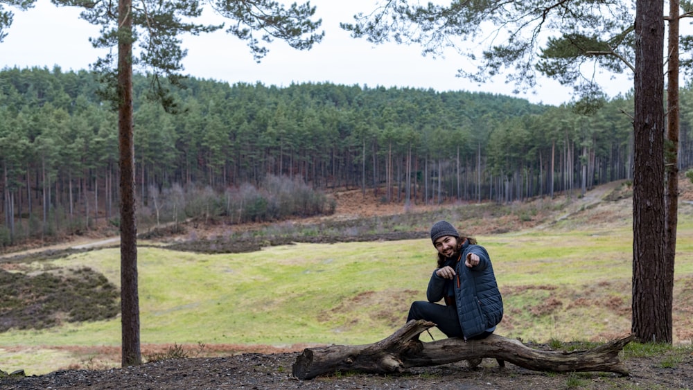 man in blue jacket sitting on tree log