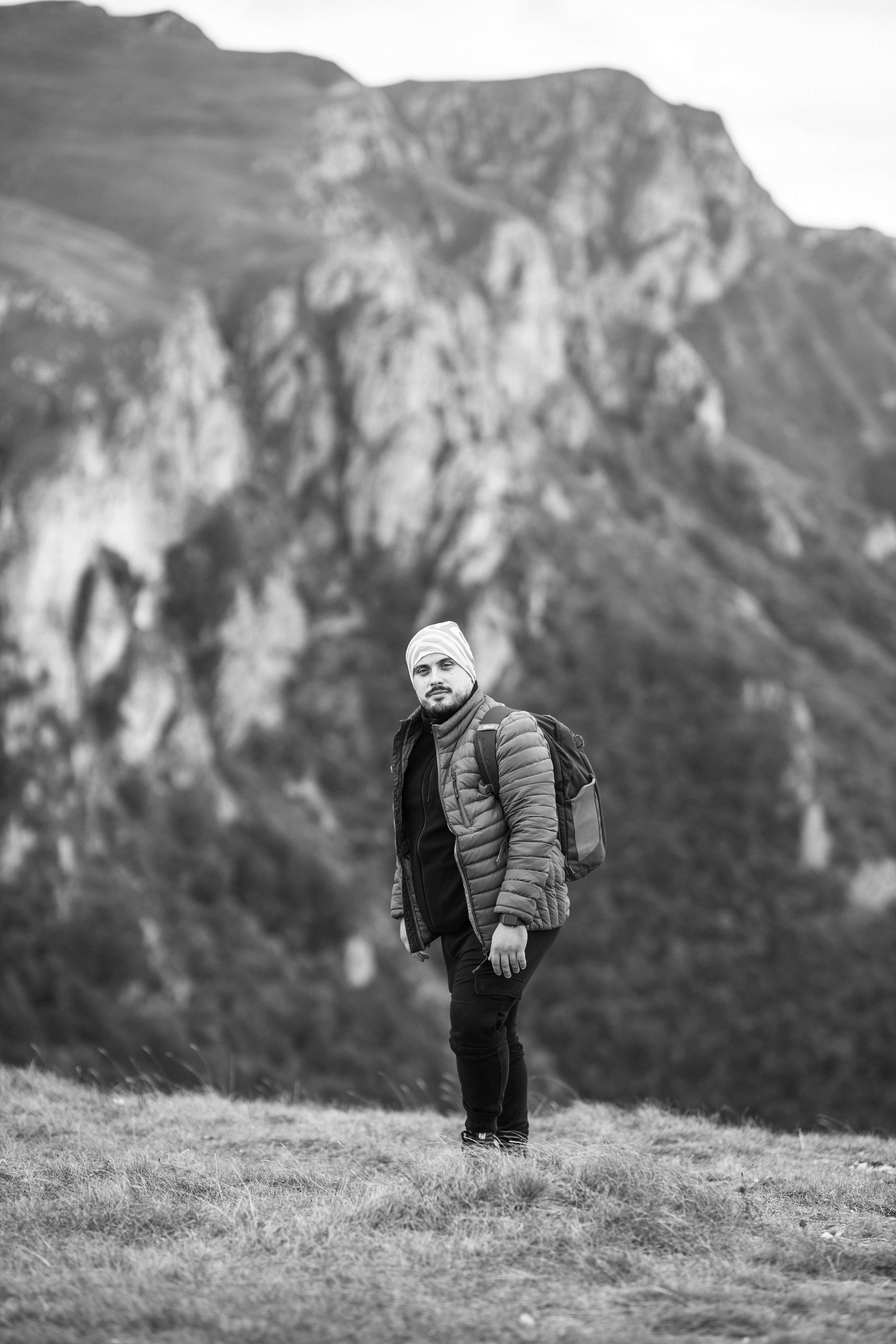 man in black jacket and black backpack standing on grass field in grayscale photography