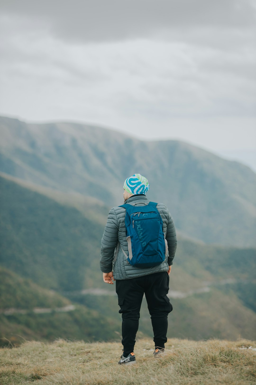 man in blue jacket and black pants with backpack standing on top of mountain during daytime