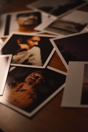 A collection of photographs scattered on a wooden surface, capturing various portraits and scenes. The lighting is dim, providing a warm and moody atmosphere.