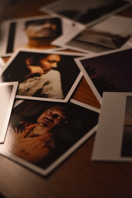 A collection of photographs scattered on a wooden surface, capturing various portraits and scenes. The lighting is dim, providing a warm and moody atmosphere.