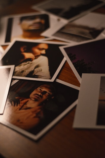 A collection of photographs scattered on a wooden surface, capturing various portraits and scenes. The lighting is dim, providing a warm and moody atmosphere.