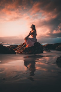 A serene woman sitting by the ocean at sunset, eyes closed, breathing deeply