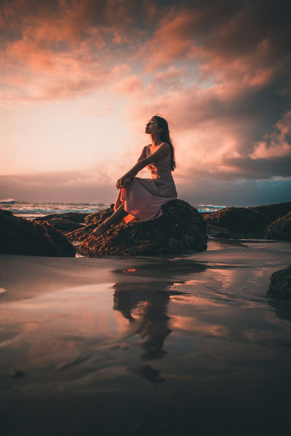 woman in white shirt and black skirt standing on rock formation near body of water during