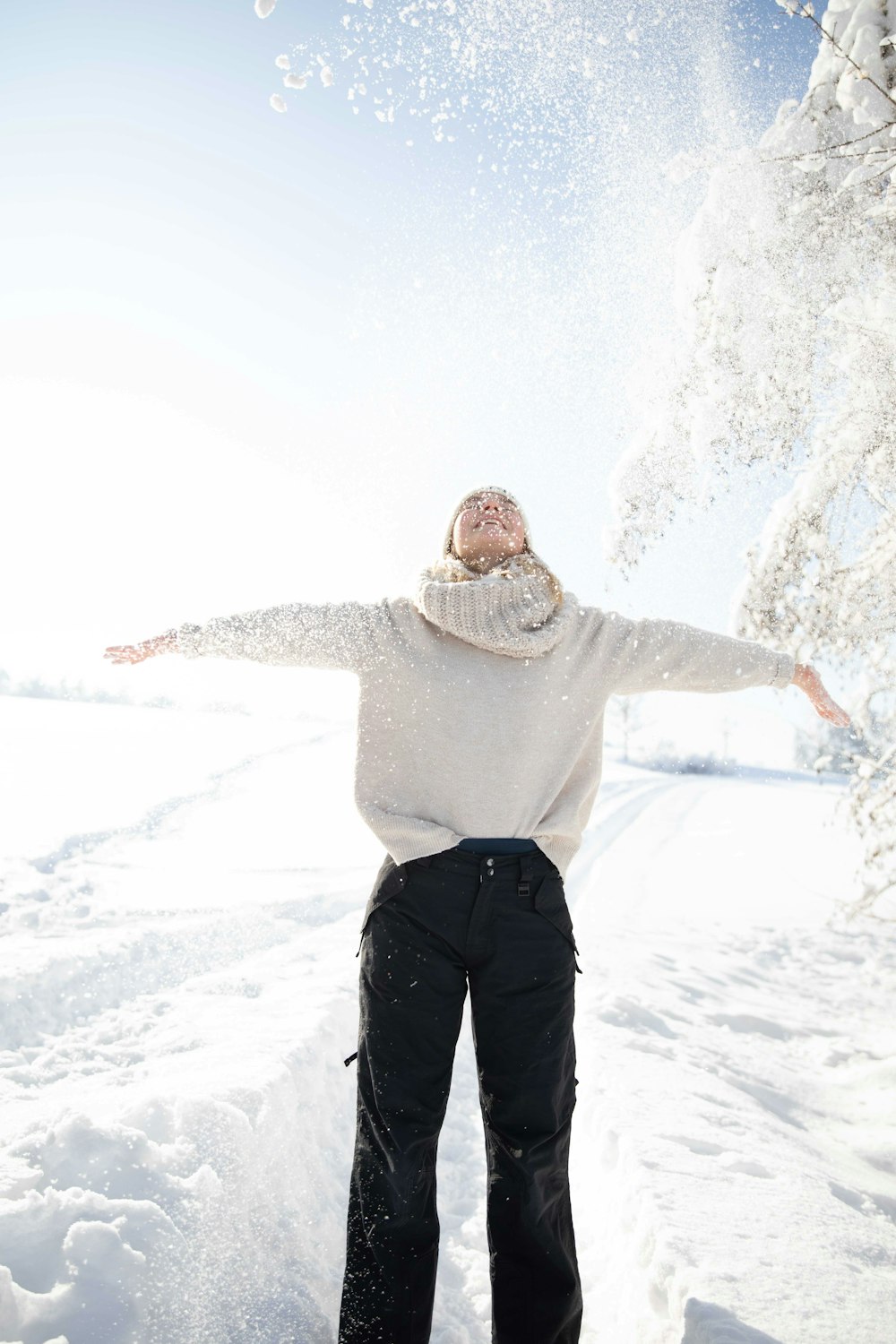 uomo in felpa con cappuccio grigia e pantaloni neri in piedi su terreno coperto di neve durante il giorno
