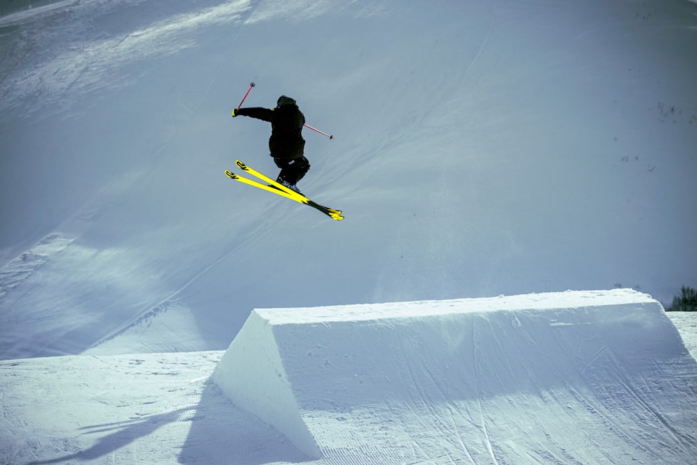 uomo in giacca nera e pantaloni gialli che cavalca lo snowboard giallo su terreno coperto di neve durante il giorno