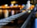 A pigeon is perched on a thick, twisted metal wire, with a background featuring bright, colorful bokeh lights, possibly from a distant cityscape. The focus is on the bird and the wire, while the lights create a warm and vibrant backdrop.