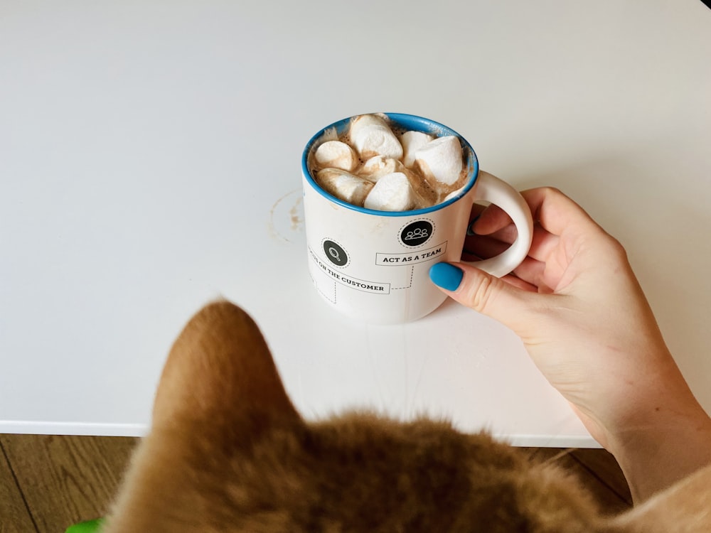 person holding white ceramic mug with brown and white dog