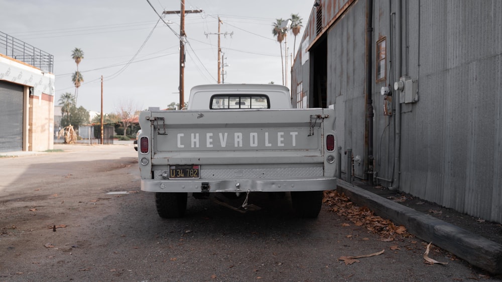 white chevrolet pickup truck parked beside brown wooden house during daytime