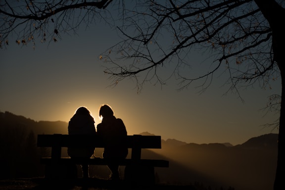 silhouette of 2 person sitting on bench during sunset
