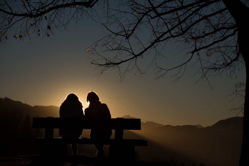 silhouette of 2 person sitting on bench during sunset