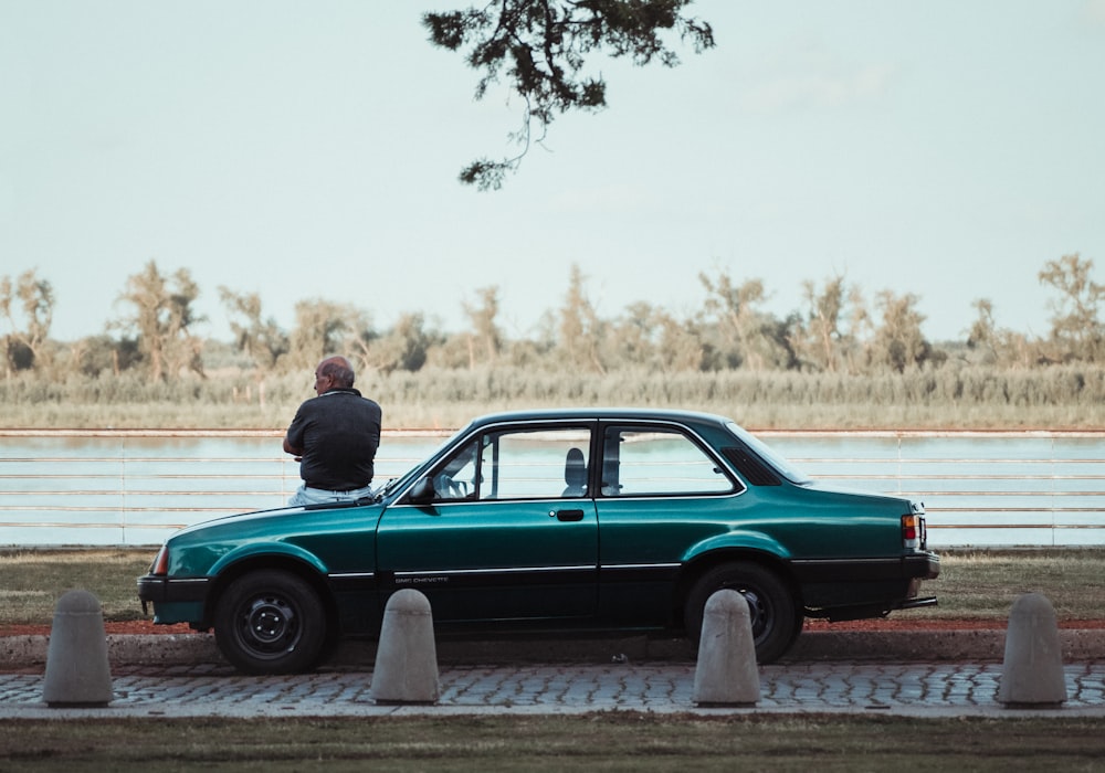 man in black jacket sitting on green car