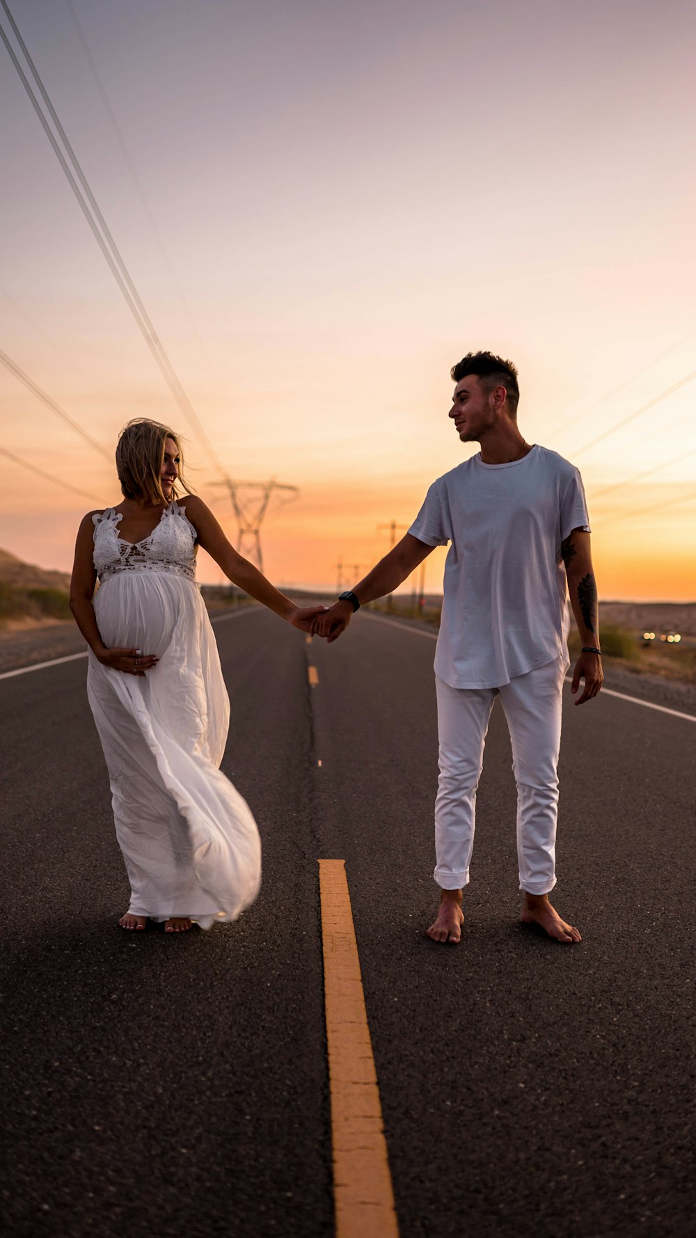 man and woman holding hands while walking on the road during sunset