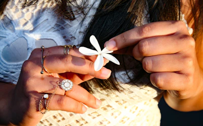 Model’s hand adorned with rings, gently holding a delicate flower.
