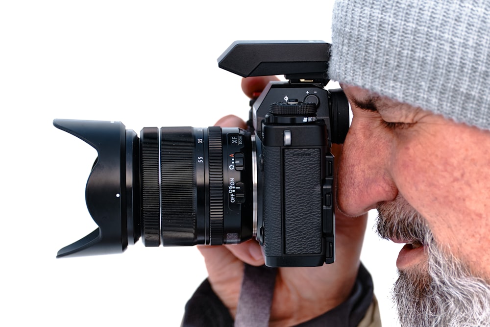 uomo in berretto a maglia grigio che tiene una fotocamera DSLR nera