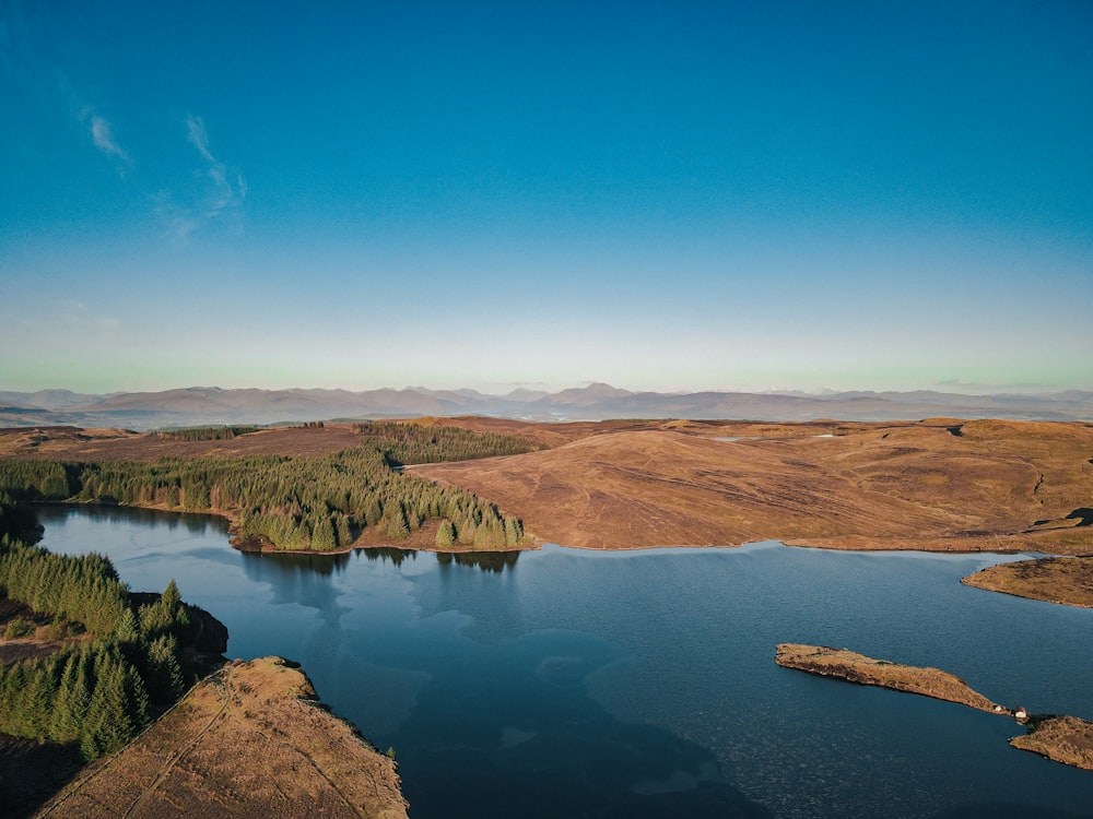 昼間の青空の下、湖畔の茶色い山々