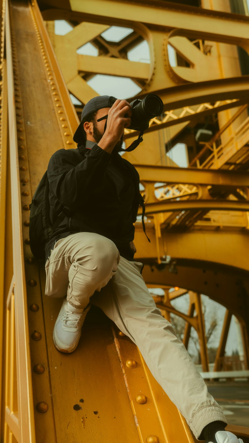 man in black jacket and white pants holding black dslr camera