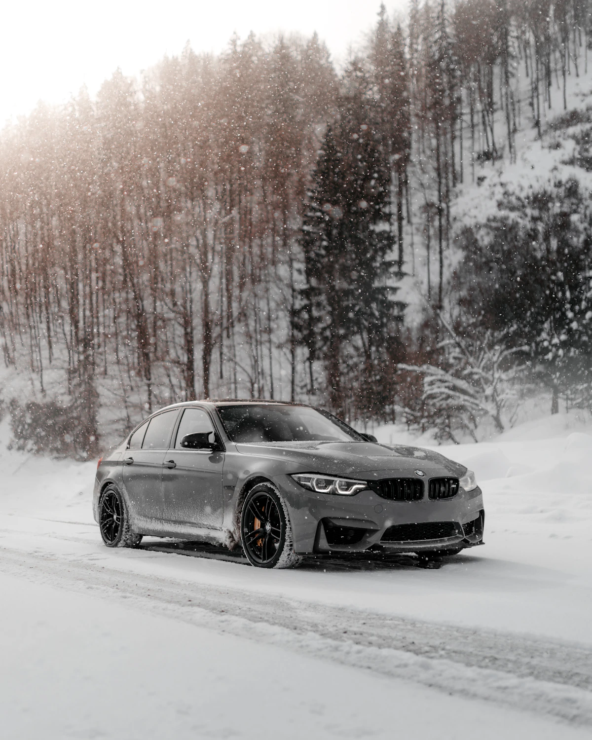 Black BMW coupe driving along a snow-covered winter road