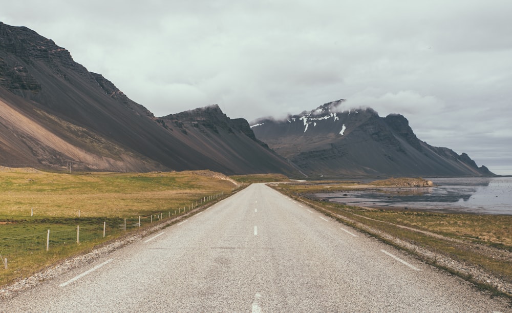 gray asphalt road near brown mountain under white sky during daytime