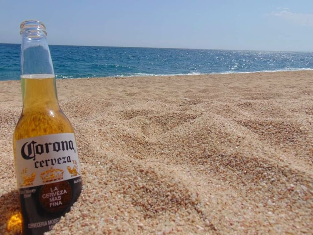 Bottiglia con etichetta marrone e bianca sulla sabbia marrone vicino al mare durante il giorno