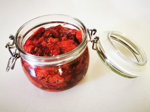 Close-up of a jar of vibrant strawberry jam with fresh strawberries around it on a wooden table.