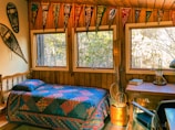 Rustic room featuring a comfortable double bed with warm blankets and forest scenery outside.