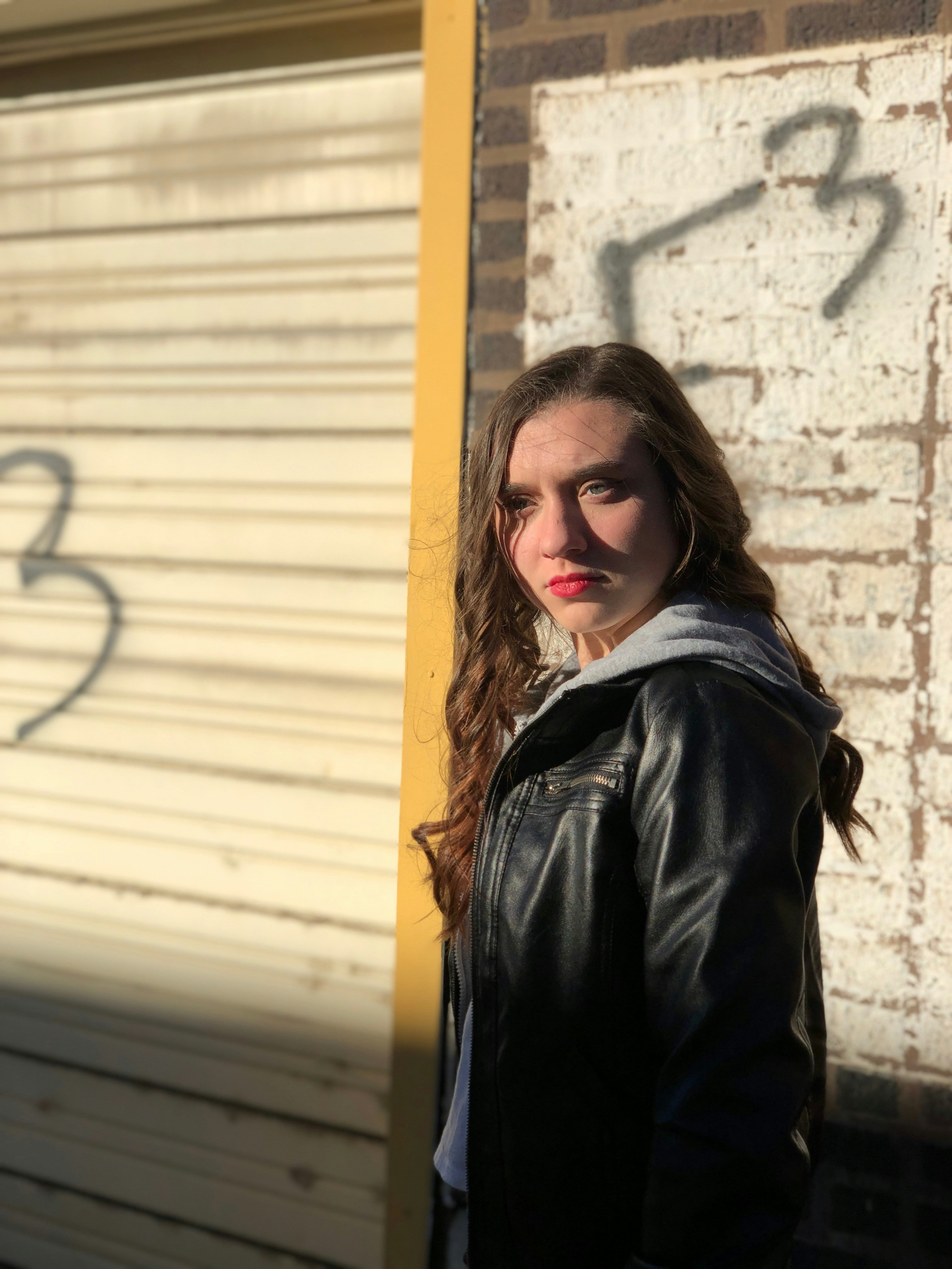 woman in black leather jacket standing beside white wall