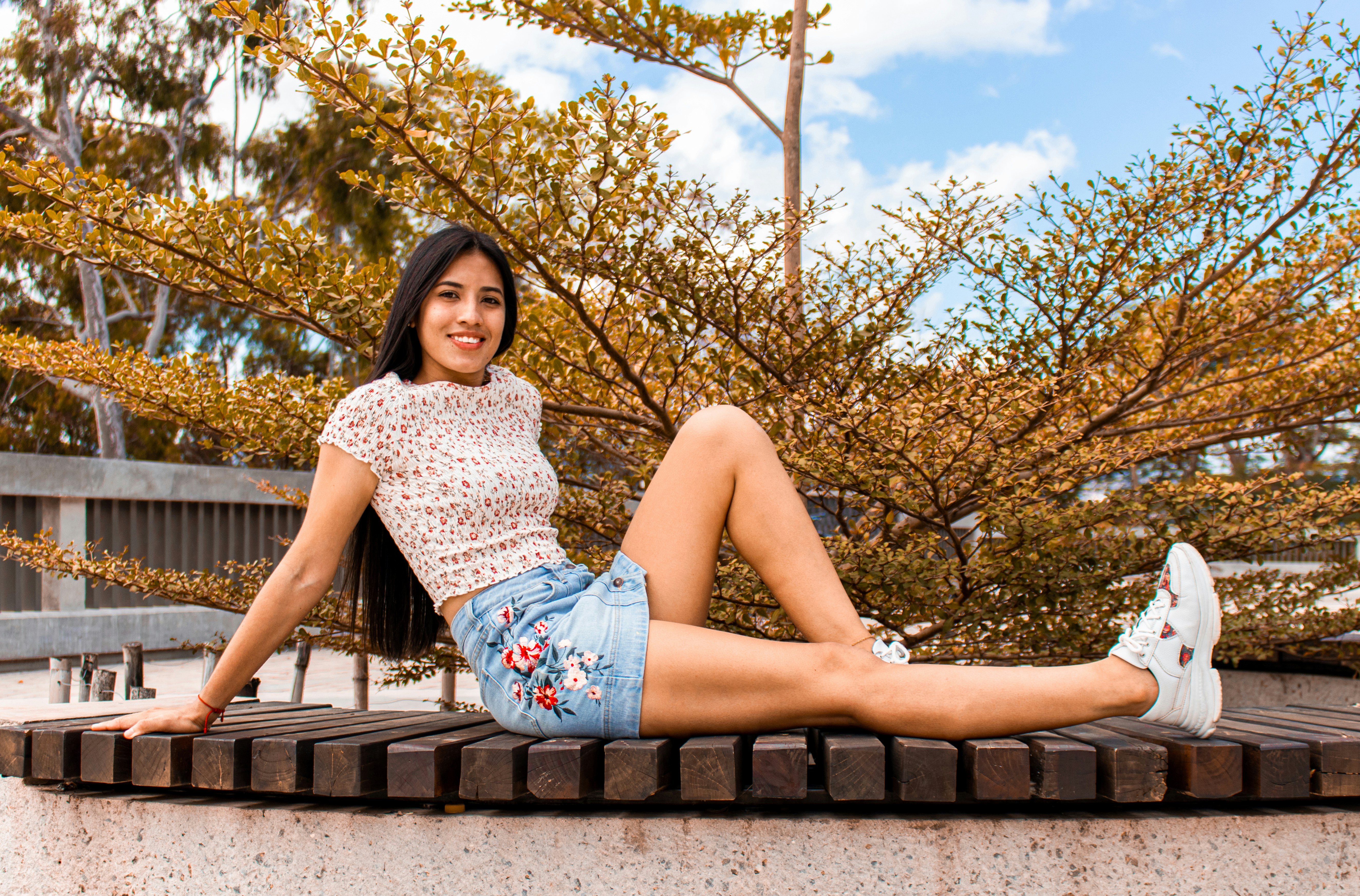 woman in white and black floral tank top and blue denim shorts sitting on brown wooden
