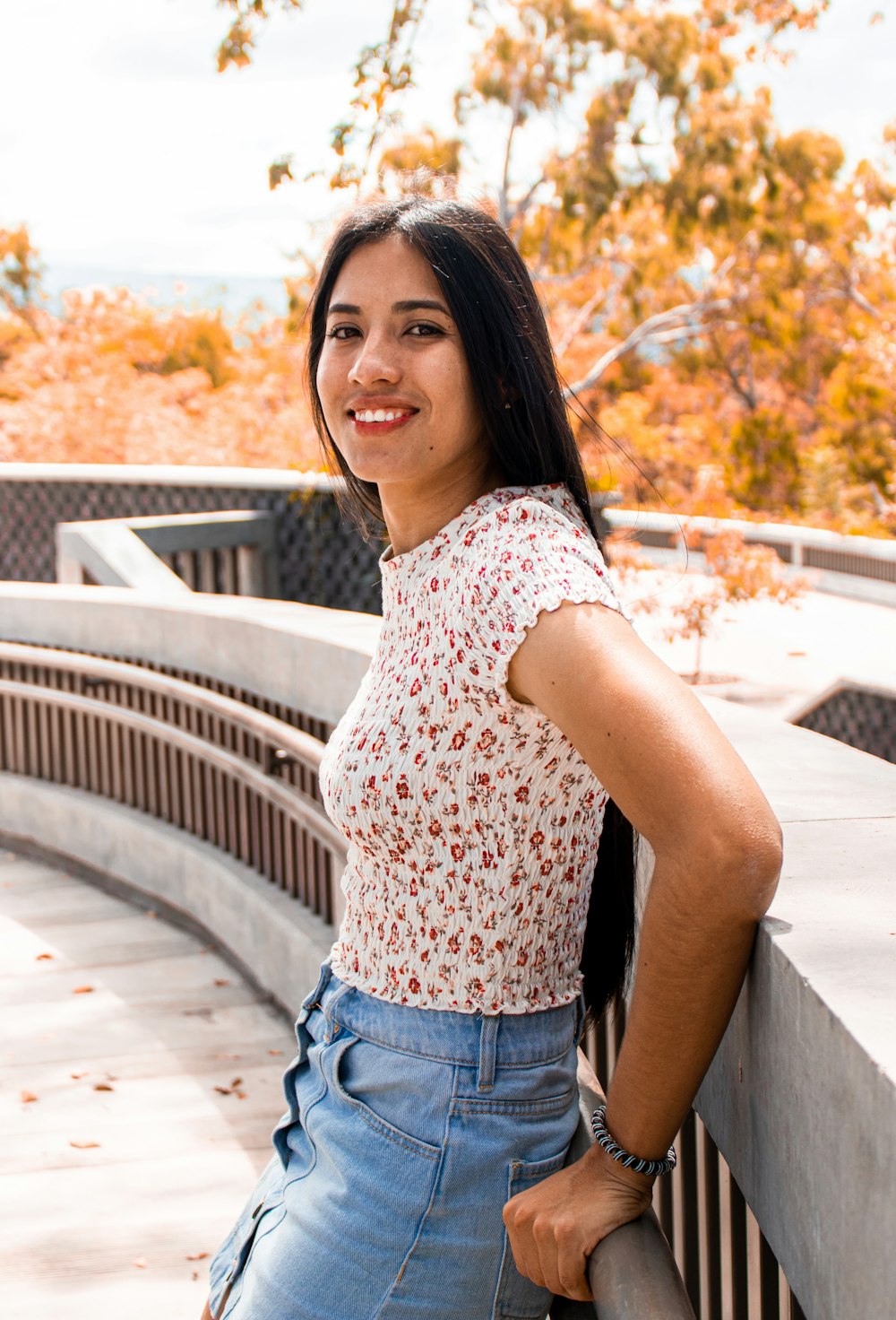 woman in white and red floral shirt and blue denim shorts standing on bridge during daytime