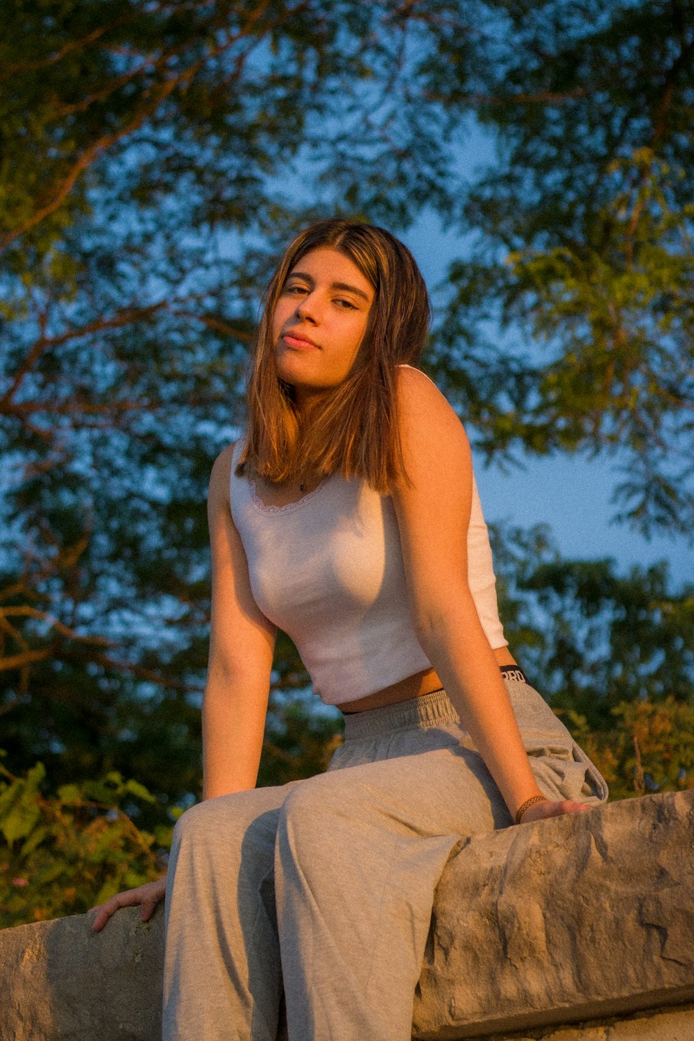 woman in white tank top and gray denim jeans sitting on brown wooden bench during daytime