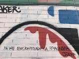 A brick wall features vibrant graffiti art with various colors. The piece includes large, sweeping curves in shades of red, blue, and green. Black spray-painted text reads 'YA HE ENCONTRADO LA PALABRA JUSTA' across the bricks.