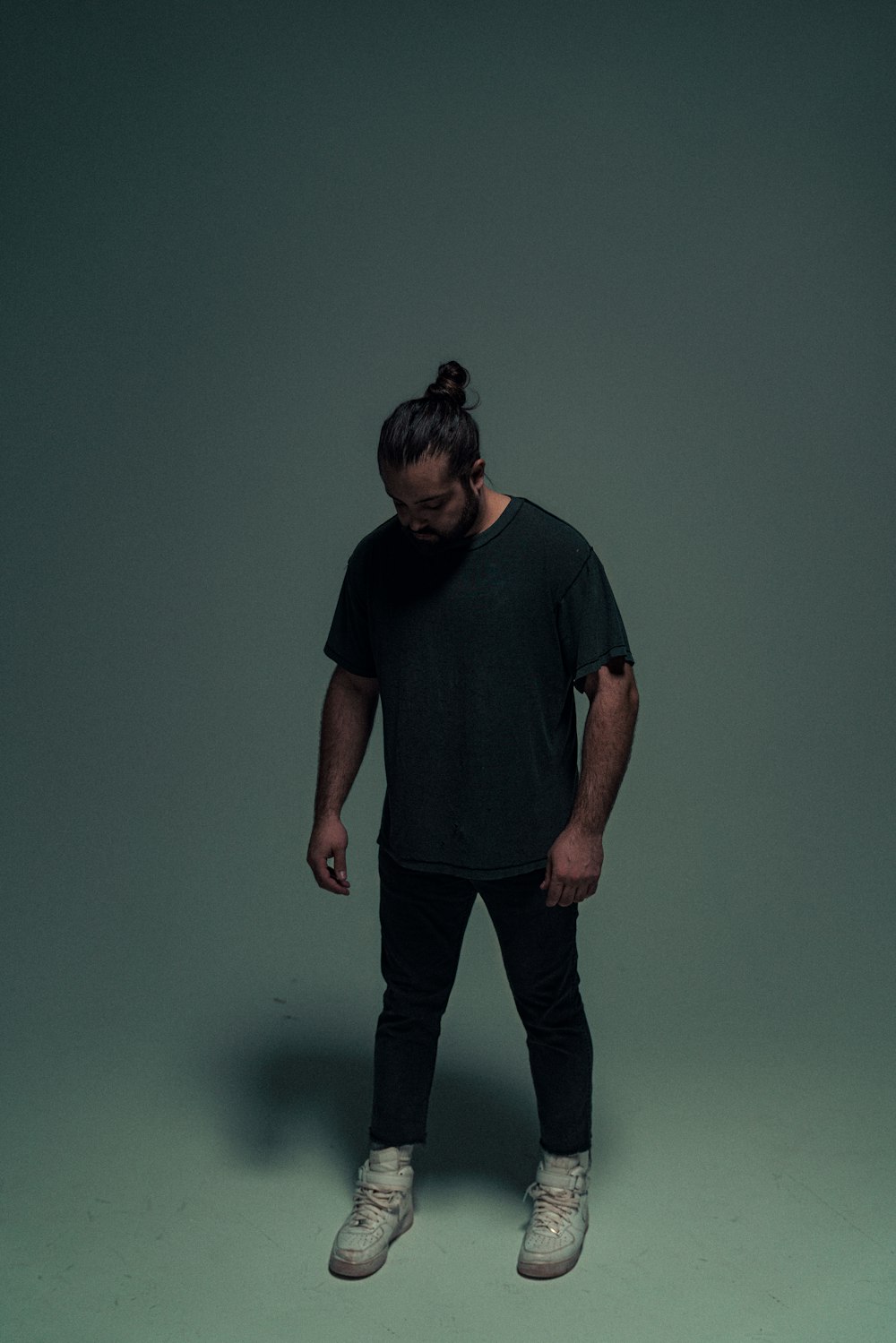 man in blue crew neck t-shirt and black pants standing beside green wall