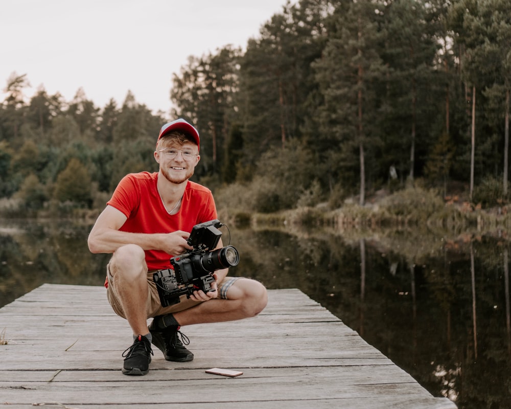 man in red crew neck t-shirt sitting on brown wooden dock during daytime