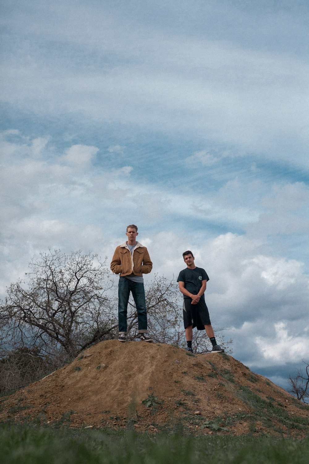 2 men standing on brown rock formation under white clouds during daytime