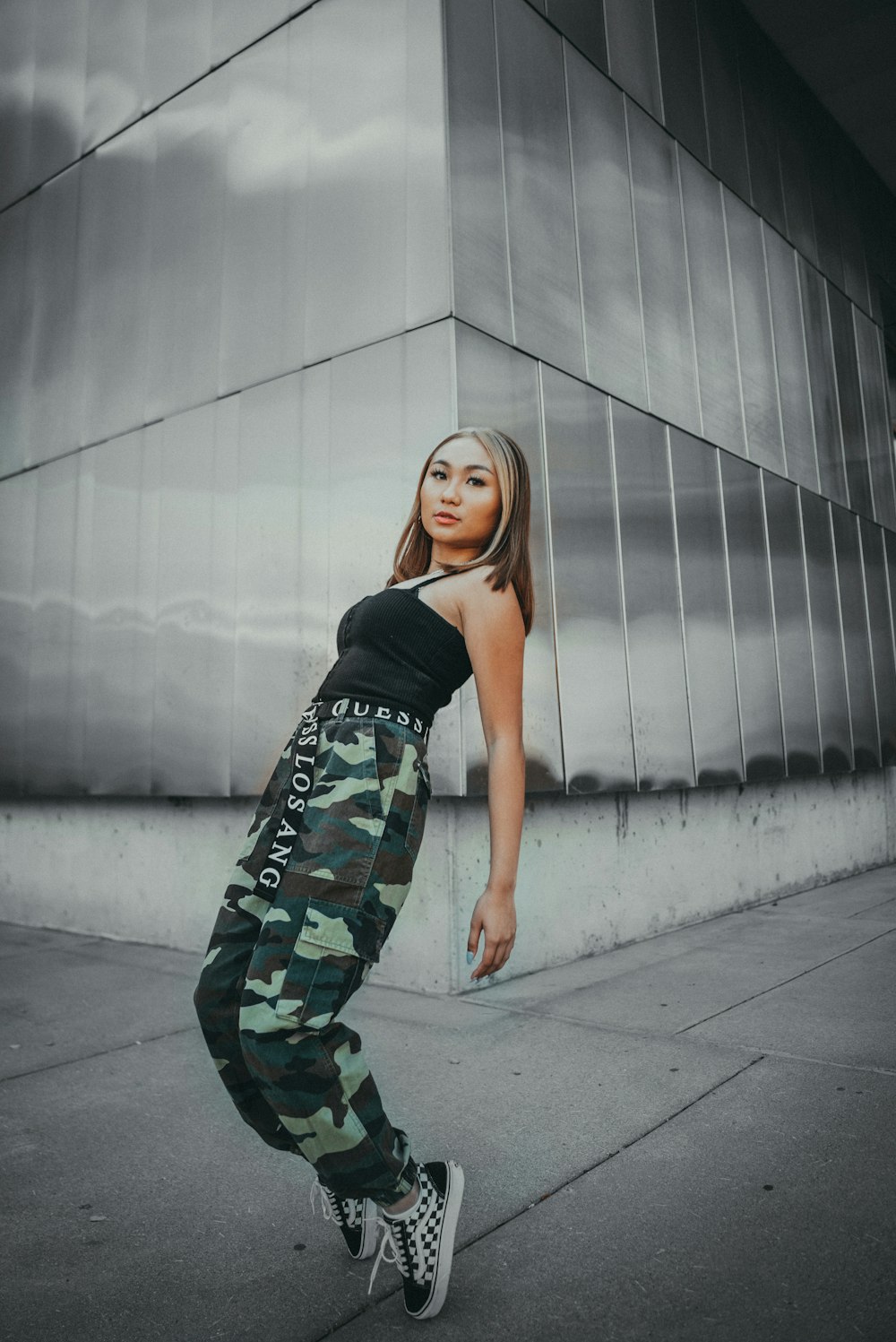 woman in black tank top and green camouflage pants standing on gray concrete floor