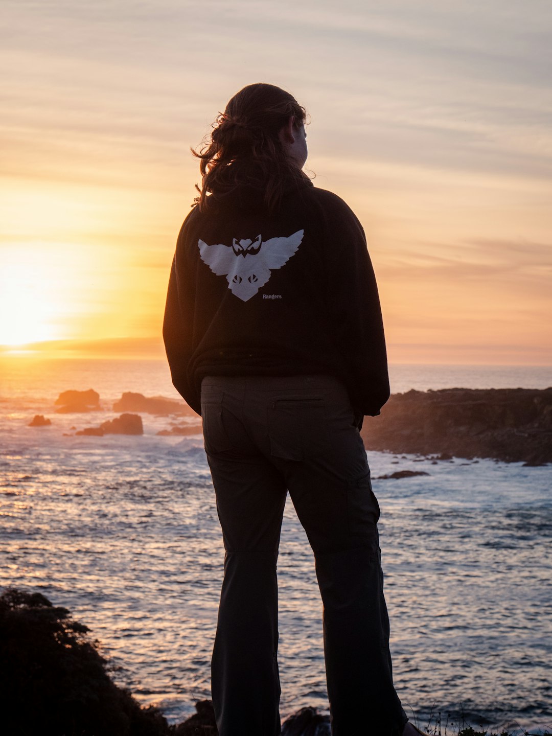 woman in black jacket standing on seashore during sunset