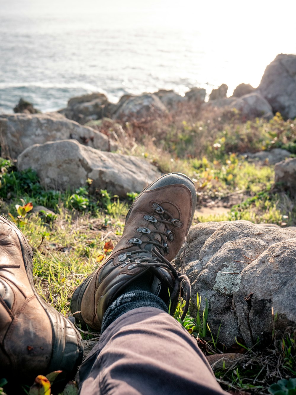 personne portant des bottes en cuir brun assise sur un rocher brun près d’un plan d’eau pendant la journée