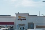 A fast-food restaurant with a prominent red and yellow sign featuring an arrow. The building has a beige facade and a red awning above the windows. Several cars are parked in front of the entrance, and there are handicap parking signs visible.
