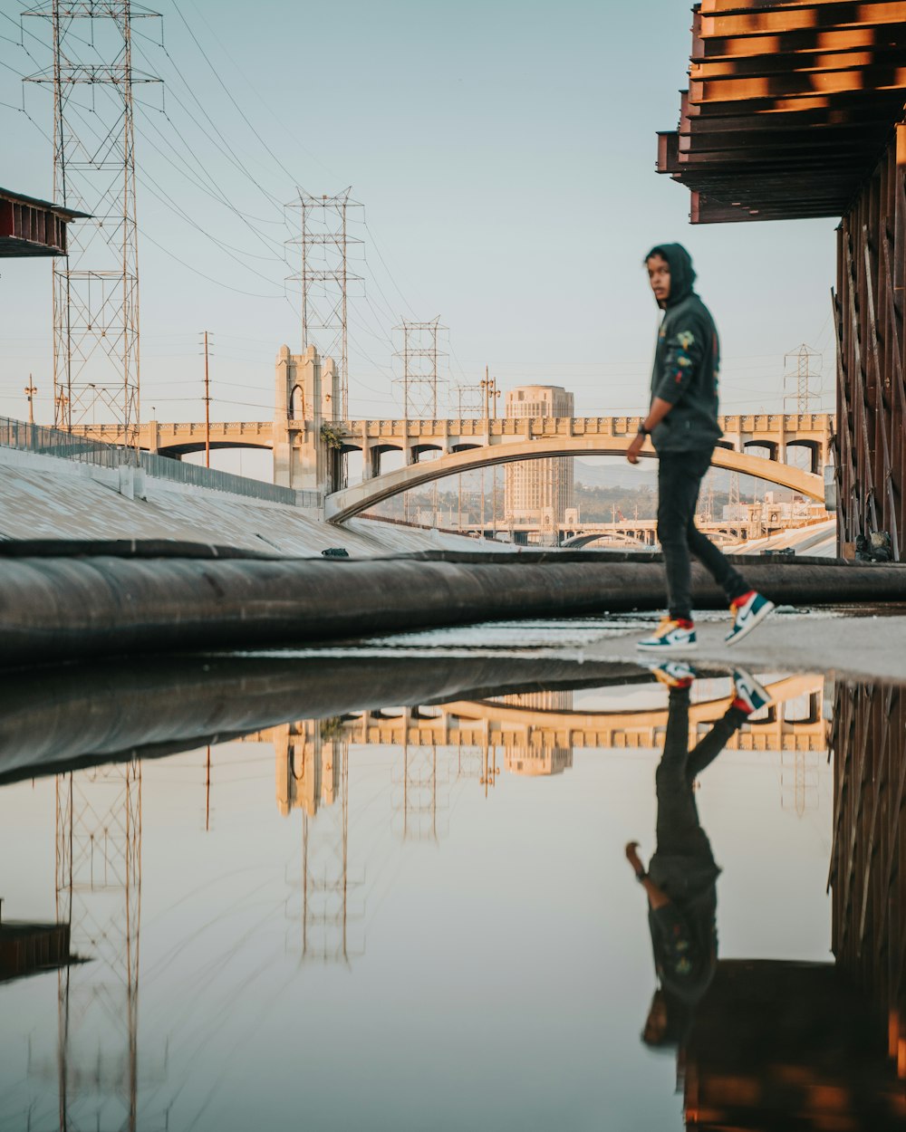 man in black jacket and black pants standing on bridge during daytime